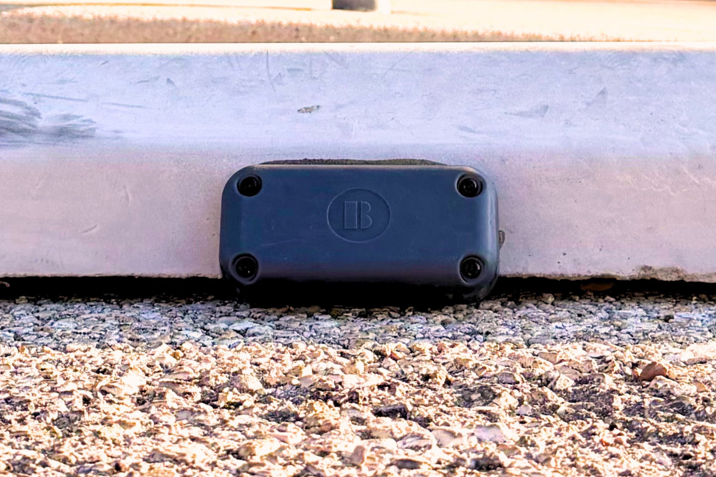 A Bizzi PS Sensor bonded to a concrete curb face, photographed at ground level.
